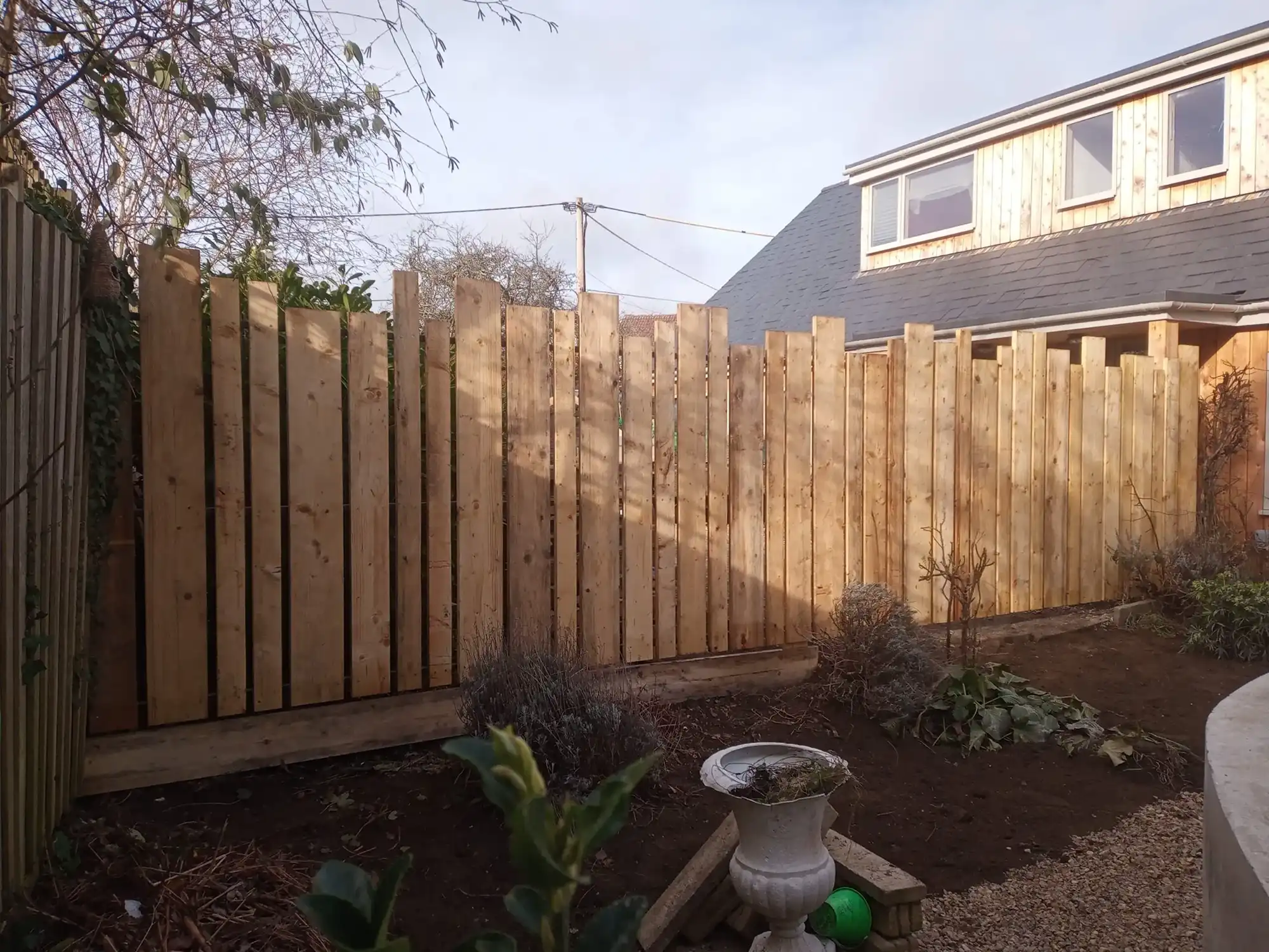 a wooden fence next to a house and a garden